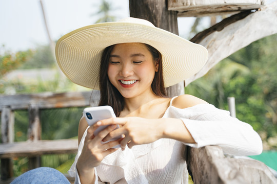 一位穿着白衬衫、戴着帽子、使用智能手机的快乐的亚洲妇女，在乡下的时候表情愉快。