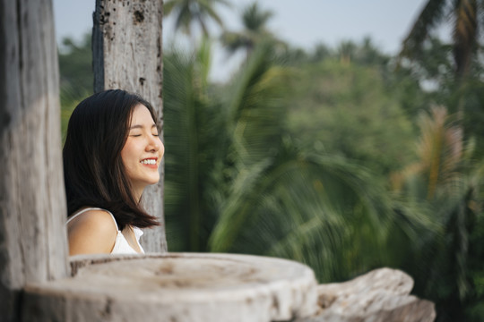 在木制乡村酒店阳台上穿着白衬衫的快乐的亚洲女人。美丽的自然背景。