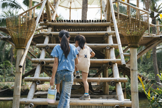 两个小女孩走上竹竿做的楼梯，拿着平托或老式食品盒。