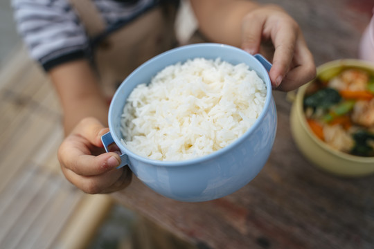小女孩手里拿着浅蓝色食物盒里的米饭。