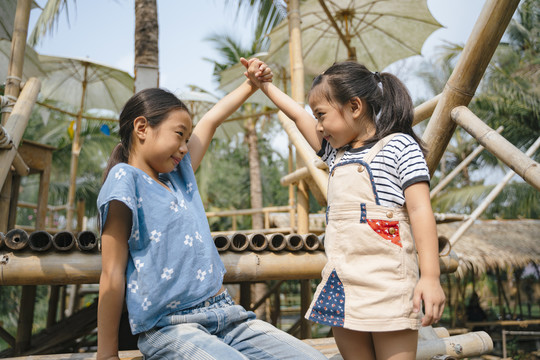 两个顽皮的亚洲小女孩手牵着手，在竹制乡村咖啡馆里旅行。