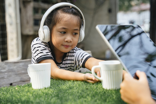 小女孩坐在公园的长椅上，用白色无线耳机听音乐。