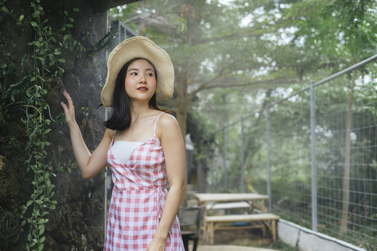 美丽的亚洲年轻女子穿着粉色连衣裙戴着大帽子在大自然中旅行。生态旅游。