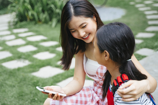 快乐的两个亚洲人妹妹喜欢坐在花园里玩智能手机。