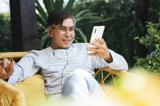 老人戴着耳机，在智能手机上听应用程序里的音乐。