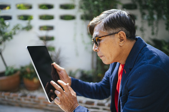 身穿蓝色西服、戴着眼镜的老人用平板电脑聚精会神地注视着股市信息。