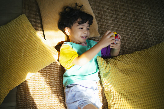 小男孩躺在地板上和许多皮洛在阳光下玩玩具。