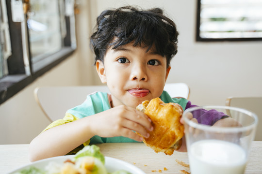 小男孩手里拿着香肠羊角面包，脸上挂着幸福的微笑。