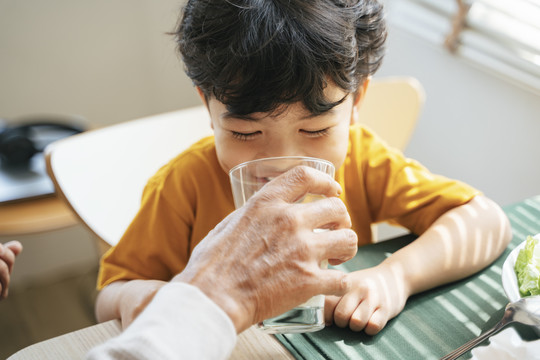 爷爷早上吃早饭时给孙子喂牛奶。