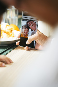 爷爷和孙子在智能手机的摄像头里，一边吃早餐一边自拍。