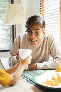 爷爷和孙子在吃早饭的时候碰了一杯牛奶。