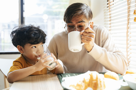 小男孩和爷爷一起喝饮料，他早上喝牛奶，爷爷喝咖啡。