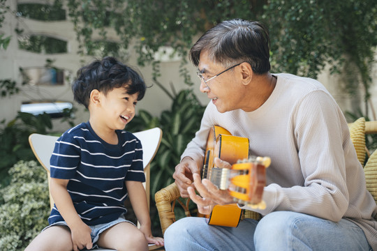 白发老人弹吉他，孙子唱歌。