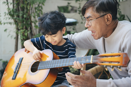 一位白发老人在他家后院教他的孙子弹吉他。