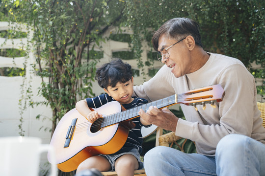 一位白发老人在他家后院教他的孙子弹吉他。