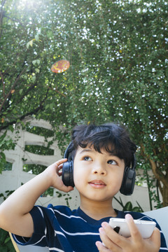 周末，戴着无线耳机的小男孩坐在后院，用智能手机看动画片。