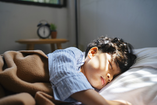 小男孩中午睡在舒适的床上，阳光从窗户射进来。