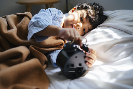 小男孩躺在床上玩古董闹钟。