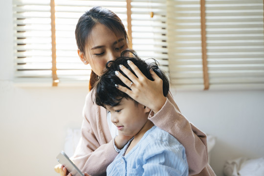 妈妈在儿子玩平板电脑游戏时亲吻他的头。