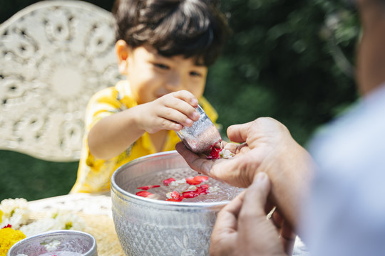 在泼水节，小男孩按照传统在爷爷的手上浇花。