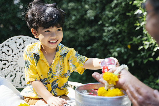 在泼水节，小男孩按照传统在爷爷的手上浇花。