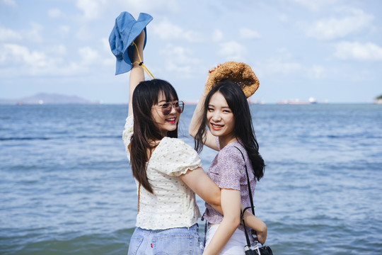 两个女孩在海边一起享受，在海边旅行，互相拥抱。