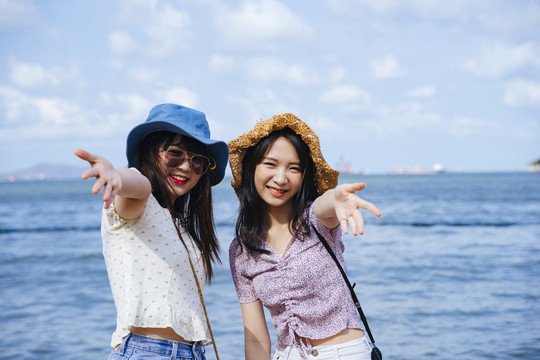 两个女孩在海边旅行时，手放在相机前，一起在沙滩上尽情享受。