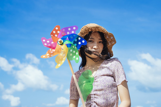 快乐可爱的女孩戴着棕色的帽子，在夏天的蓝天白云下，在风和日丽的日子里捧着五颜六色的风车。