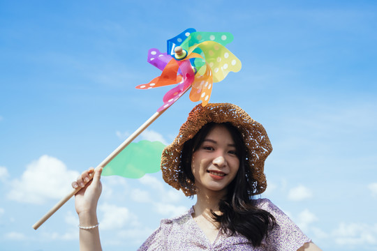快乐可爱的女孩戴着棕色的帽子，在夏天的蓝天白云下，在风和日丽的日子里捧着五颜六色的风车。