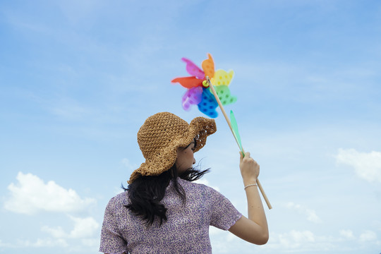 背照：戴着棕色帽子的可爱女孩手持风车在蓝天下随风旋转。