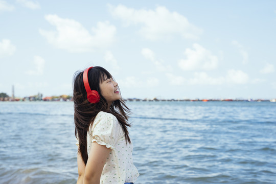 风和日丽的海边，可爱的女孩戴着红色的无线耳机欣赏着音乐。