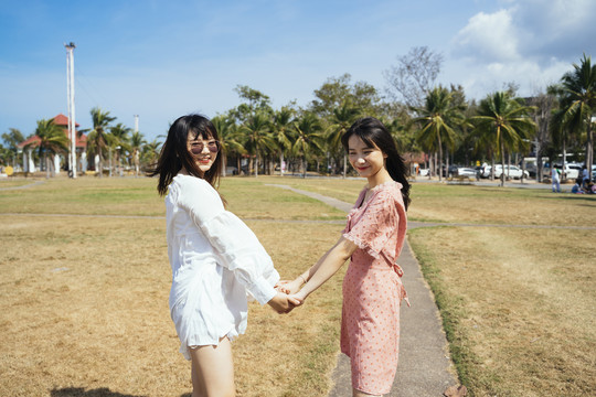 在夏日的阳光下，两个女孩手牵着手在草地上散步玩耍。