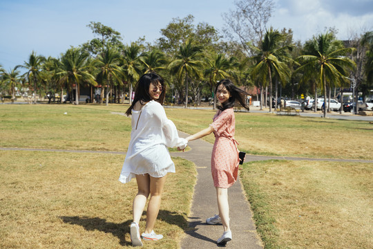 在夏日的阳光下，两个女孩手牵着手在草地上散步玩耍。