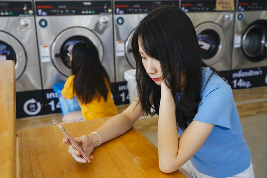 无聊的女孩一边在洗衣机里等衣服，一边滚动着智能手机屏幕。