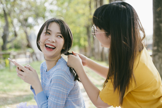 黄色t恤女孩在野餐时为蓝色t恤女孩做发型设计。