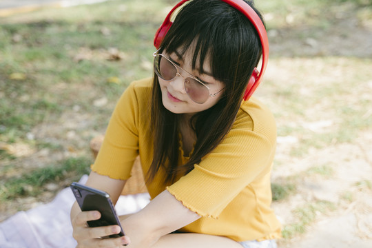 戴着墨镜和红色耳机的黄色t恤女孩在智能手机应用程序中选择音乐。