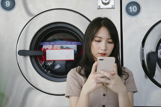 长空女孩在洗衣机前使用智能手机。