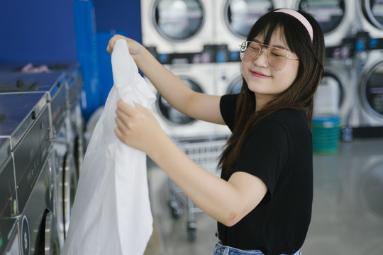 可爱的女孩看着洗衣机里的衣服，微笑着说她的衣服很干净。
