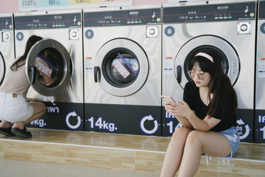 戴眼镜的长发女孩在等待洗衣机时使用智能手机。