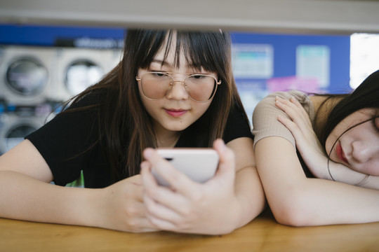 戴墨镜的女孩在朋友睡觉时用智能手机。