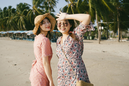 风大的时候，两个可爱的女孩和椰子树在沙滩上漫步。