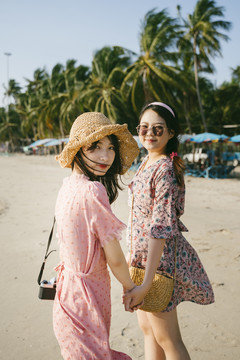 风大的时候，两个可爱的女孩和椰子树在沙滩上漫步。