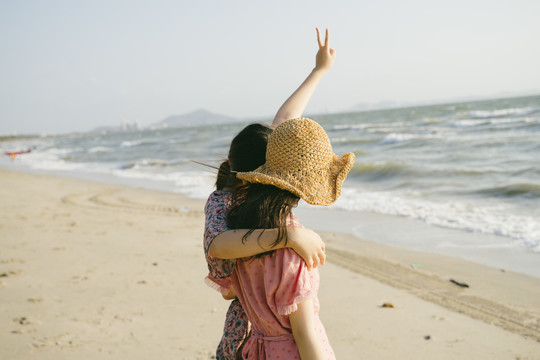 两个女孩站在沙滩上，互相拥抱，向天空伸出胜利之手。