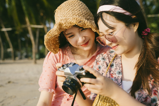 两个女孩坐在沙滩上，看着这次旅行的照片。