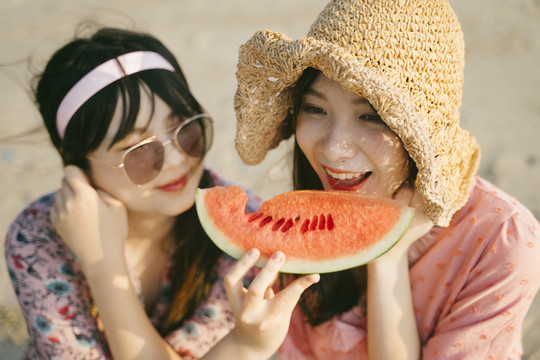 戴墨镜的女孩坐在沙滩上给她的朋友喂西瓜。