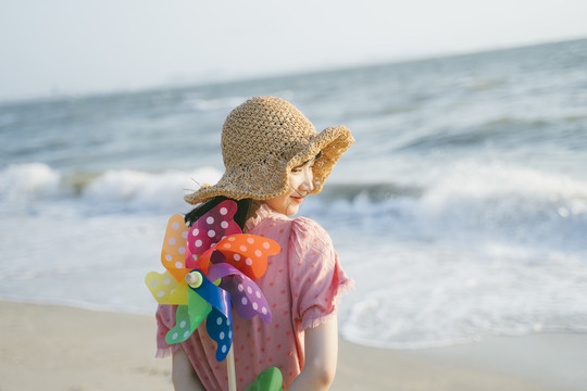 可爱的女孩站在沙滩上，身后是五颜六色的风车。