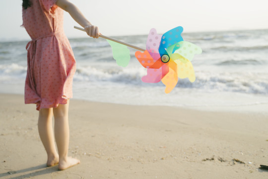 站在海滩上的女孩手中五颜六色的风车的剪影。