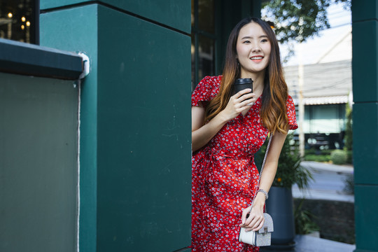 街上的绿墙，一位穿着红裙子的亚洲年轻女子手里拿着一杯咖啡。