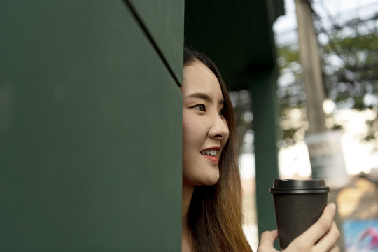 特写：穿着红色连衣裙的亚洲年轻女子喜欢在街上喝咖啡。