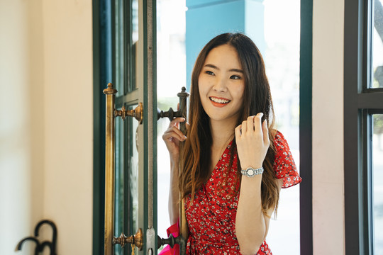 一位身着红色连衣裙的亚洲年轻女子站在门口，兴高采烈地走进老式咖啡馆。